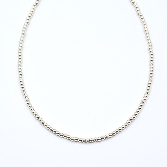 Close-up of gold filled beaded choker necklace showing minimalist chain detail on white background