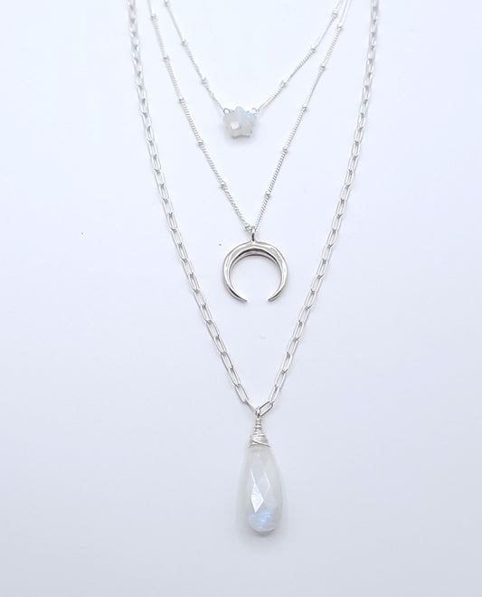 Layered sterling silver celestial necklace stack featuring moonstone necklaces, a crescent luna pendant, and a faceted moonstone drop pendant on a soft light gray background