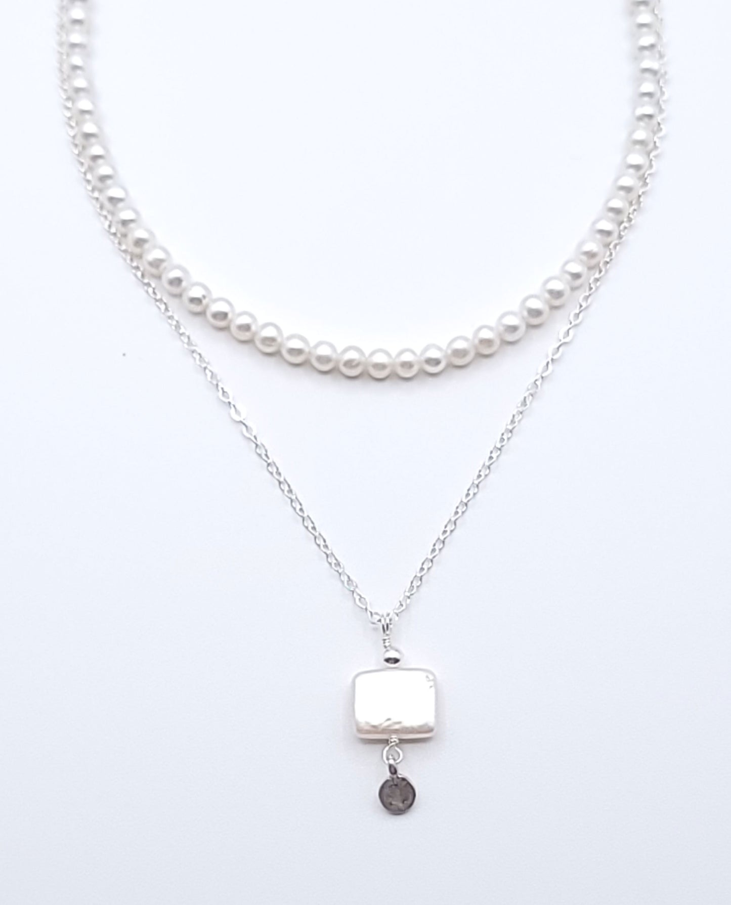 Layered sterling silver pearl necklace stack featuring the Quiet Light pendant necklace with mother of pearl on a soft light gray background