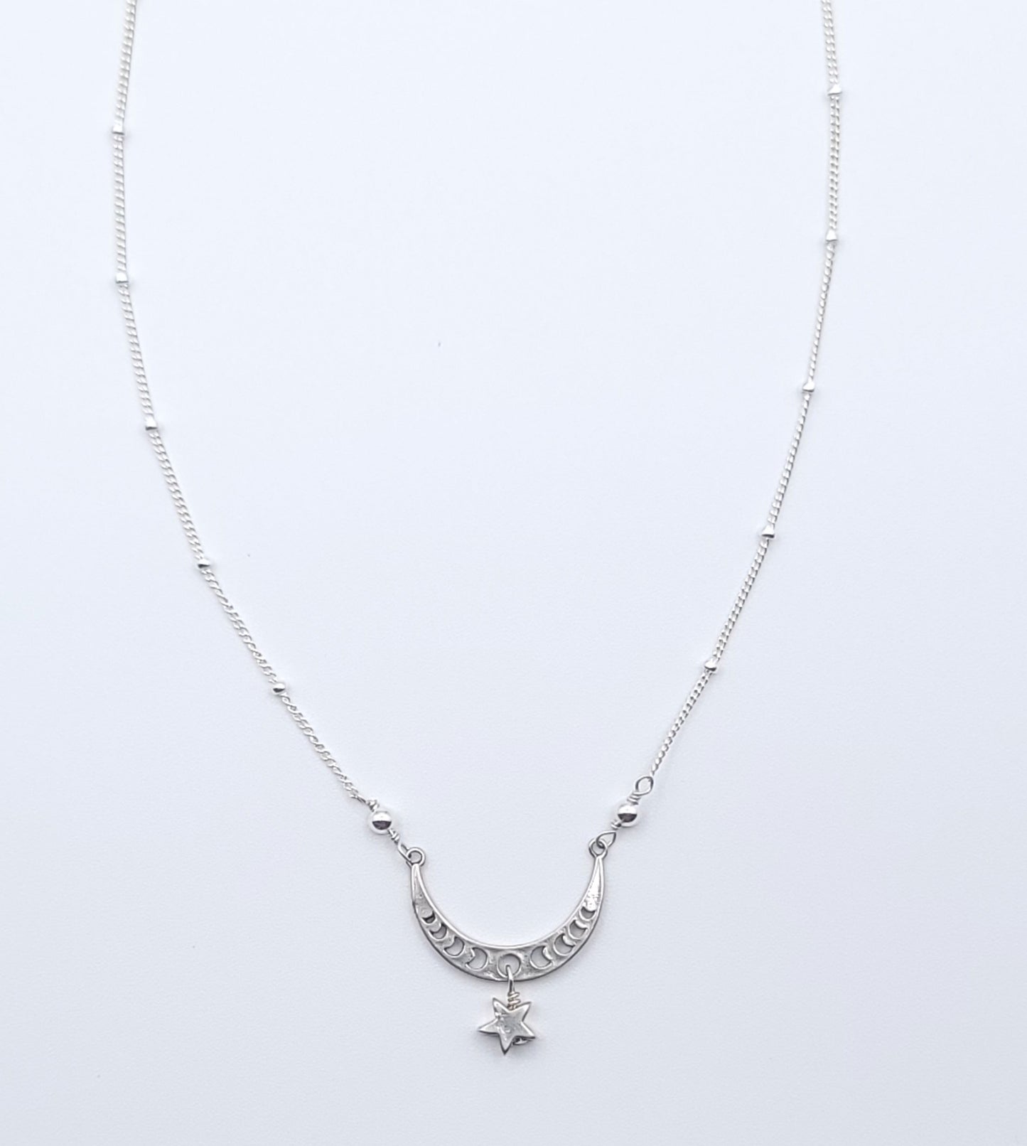 Sterling silver crescent moon necklace with star charm pendant, full view in celestial minimalist style on light background