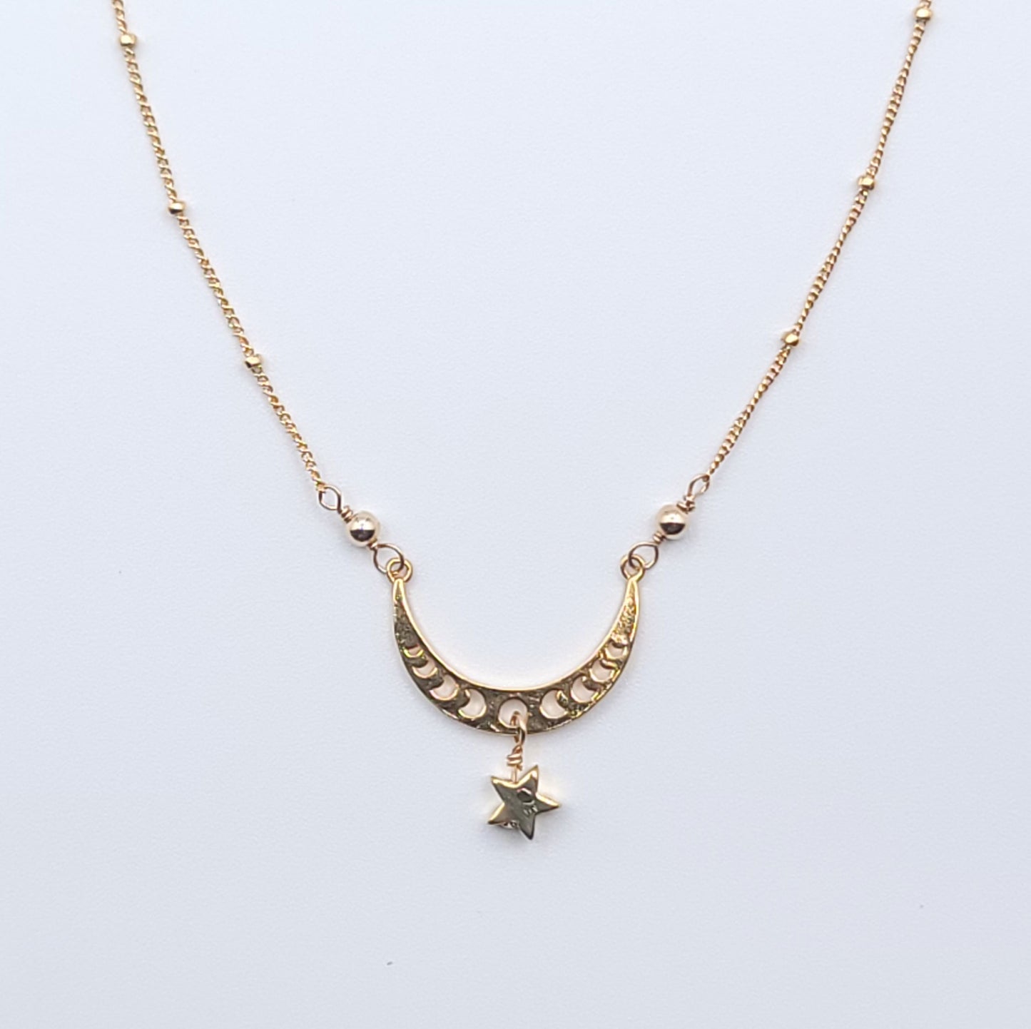 Gold crescent moon necklace with star charm pendant in celestial minimalist style on light background