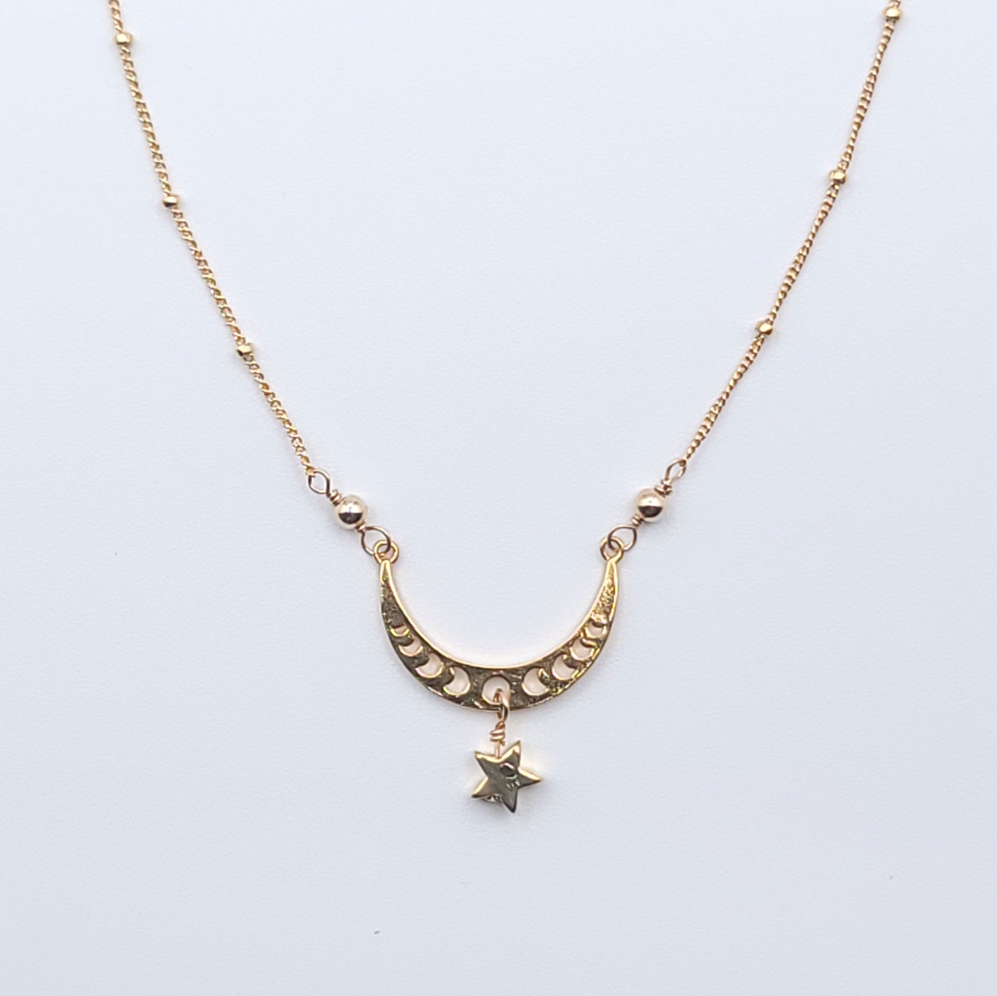 Gold crescent moon necklace with star charm pendant in celestial minimalist style on light background