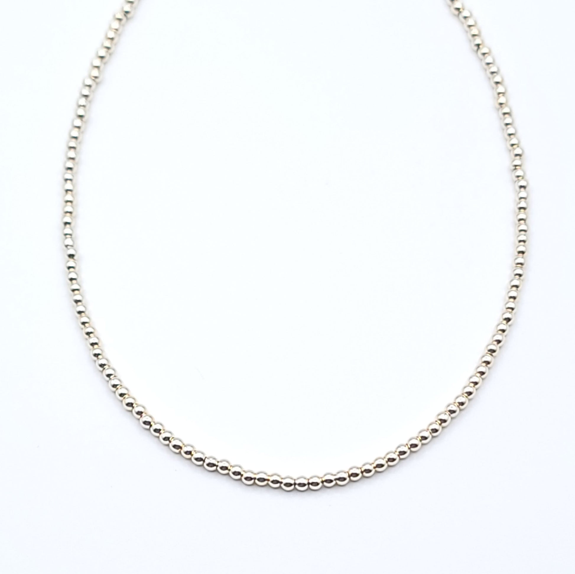 Close-up of gold filled beaded choker necklace showing minimalist chain detail on white background