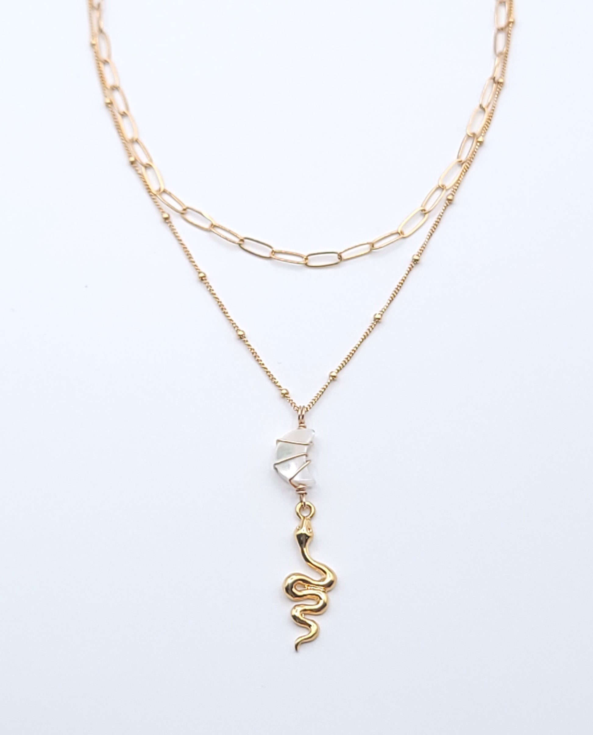 Layered gold-filled necklace stack featuring the Essential Chain Necklace and Snake Charmer Necklace with a mother of pearl crescent moon pendant on a soft light gray background