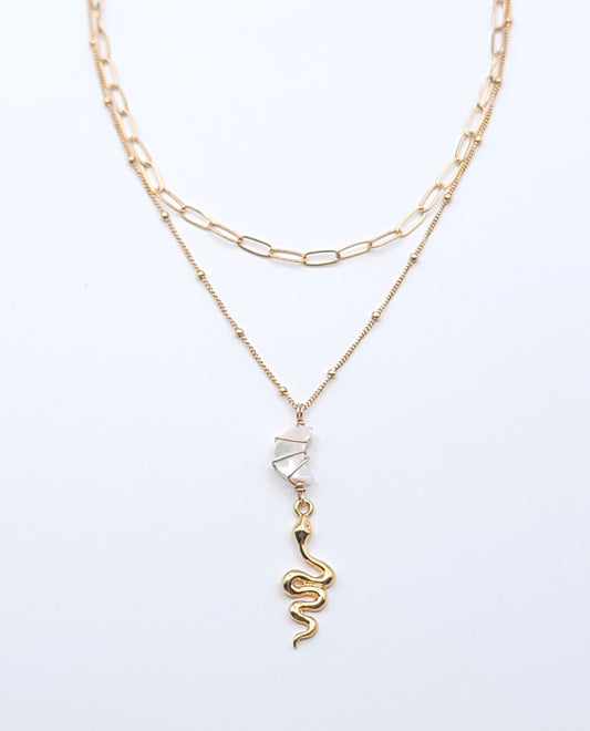 Layered gold-filled necklace stack featuring the Essential Chain Necklace and Snake Charmer Necklace with a mother of pearl crescent moon pendant on a soft light gray background
