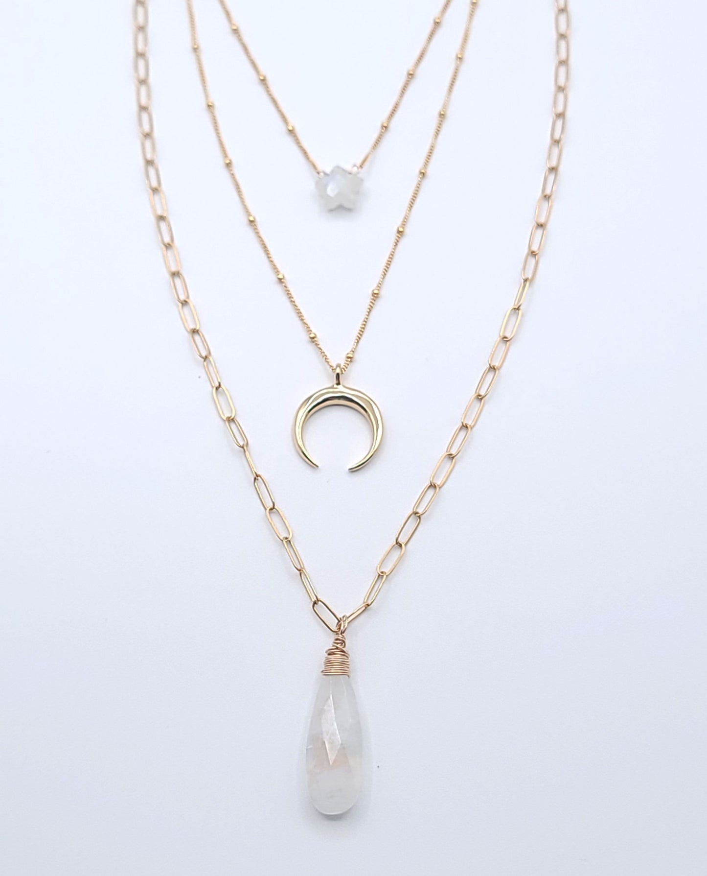 Layered gold-filled celestial necklace stack featuring moonstone necklaces, a crescent luna pendant, and a faceted moonstone drop pendant on a soft light gray background