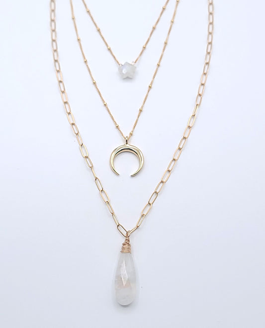 Layered gold-filled celestial necklace stack featuring moonstone necklaces, a crescent luna pendant, and a faceted moonstone drop pendant on a soft light gray background