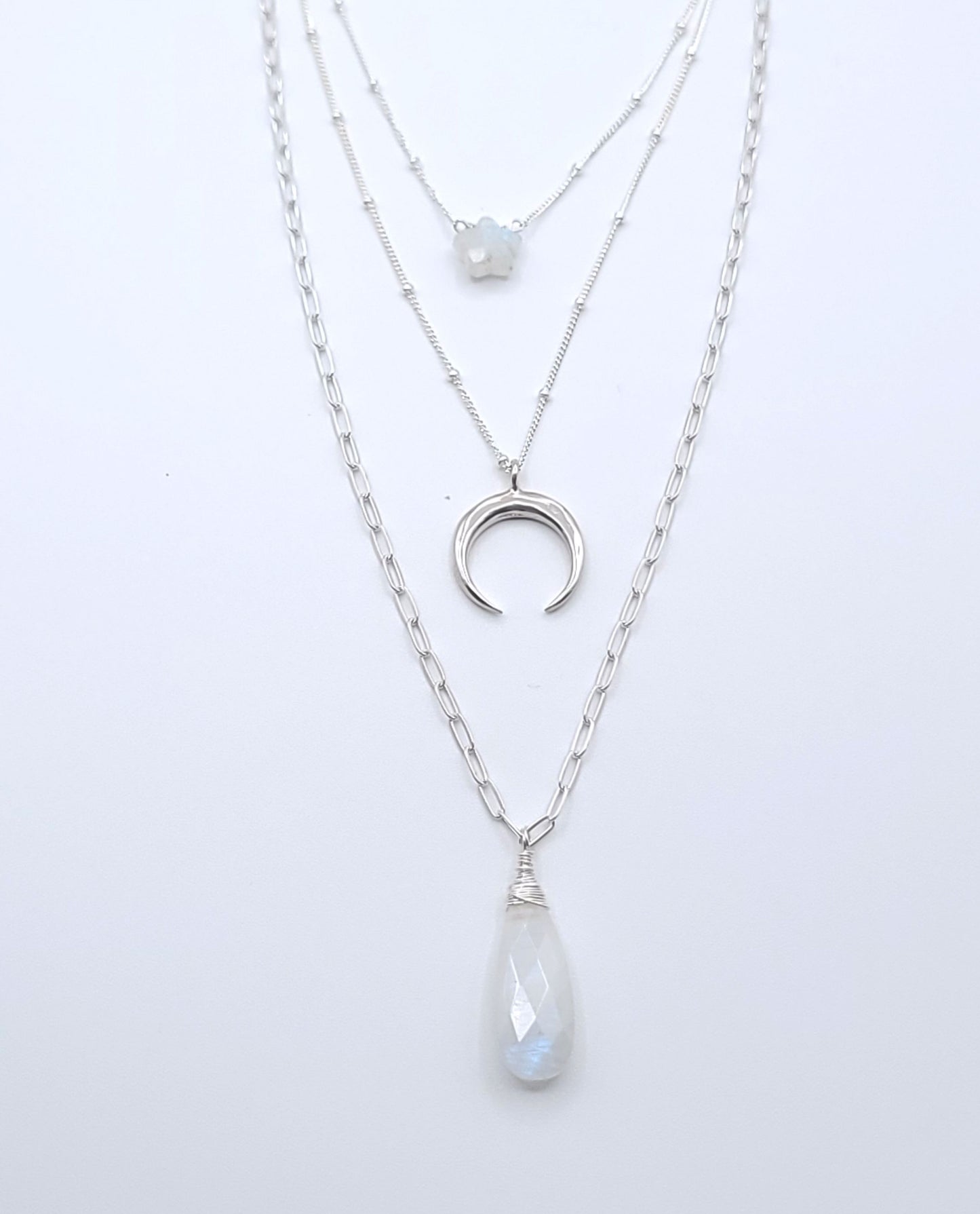 Layered sterling silver celestial necklace stack featuring moonstone necklaces, a crescent luna pendant, and a faceted moonstone drop pendant on a soft light gray background