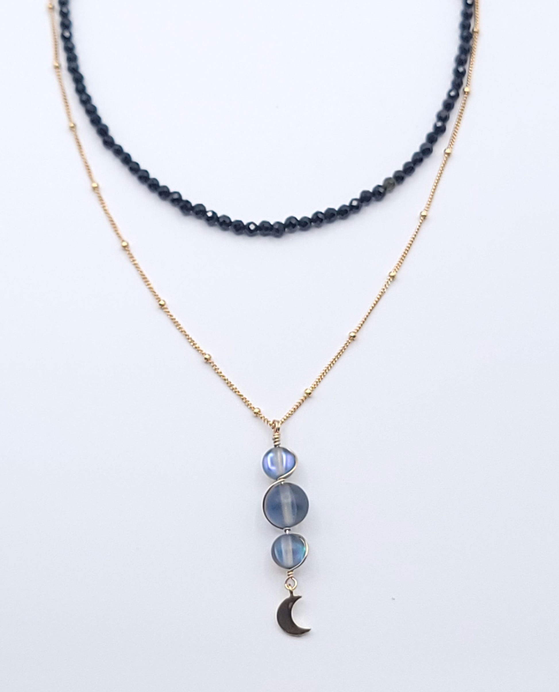 Layered gold-filled midnight necklace stack featuring the Moon Phases Silver Aura necklace and Boundless Protection choker on a soft light gray background