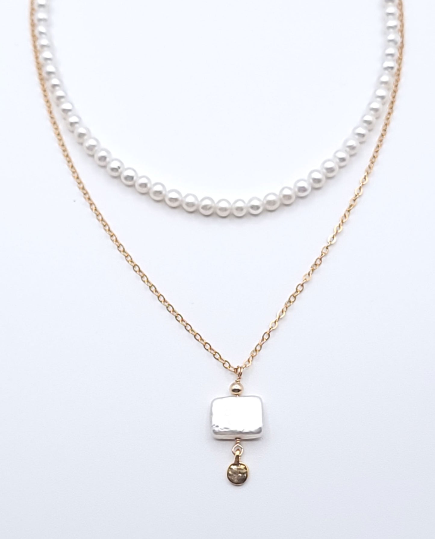 Layered gold-filled pearl necklace stack featuring the Quiet Light pendant necklace with mother of pearl on a soft light gray background